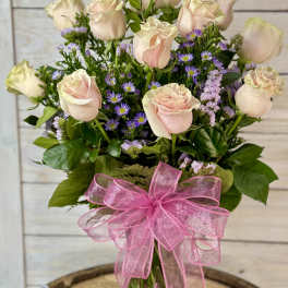 Bouquet of pale pink roses and purple filler flowers in a glass vase with a pink ribbon