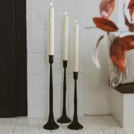 Three tall white taper candles in black holders on a hearth