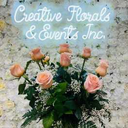 Pink roses arranged before a white floral wall with a glowing sign