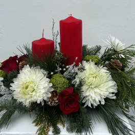 Red candles in a floral arrangement with white blooms and evergreen accents