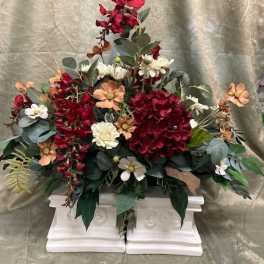 Red and peach floral arrangement in a white pedestal container