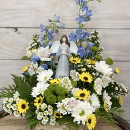 Basket arrangement with white and yellow flowers and a small angel figurine
