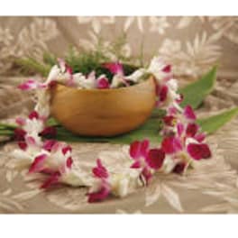 Pink and white orchid lei draped around a wooden bowl