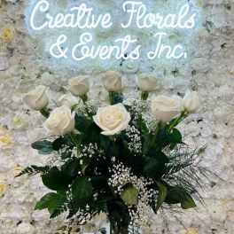 White rose bouquet in a glass vase before a floral wall sign