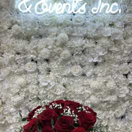 Red rose bouquet in front of a white floral wall with a glowing sign