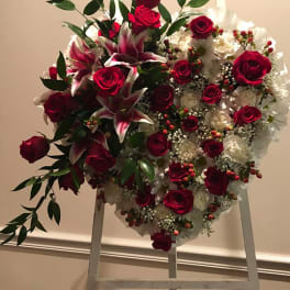 Heart-shaped floral wreath with red roses and white lilies on an easel