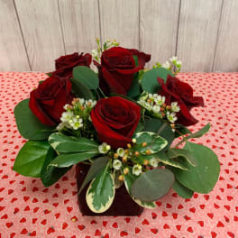 Red roses arranged in a low vase with mixed greenery and small white filler flowers