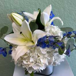 White lilies and blue flowers arranged with white hydrangeas in a vase