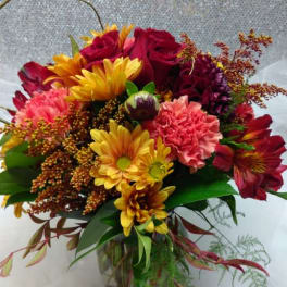 Mixed bouquet of red roses, yellow daisies, and pink carnations in a glass vase