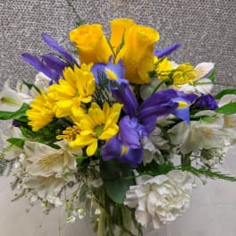 Bouquet of yellow roses, purple irises, and white flowers in a glass vase