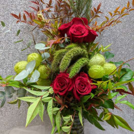 Red roses arranged in a glass vase with mixed greenery and green fuzzy accents