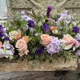 Low floral arrangement with peach roses and purple blooms in a wooden box