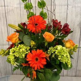 Orange gerbera daisies and roses in a clear glass vase