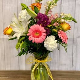 Mixed bouquet of pink, white, purple, and orange flowers in a glass vase