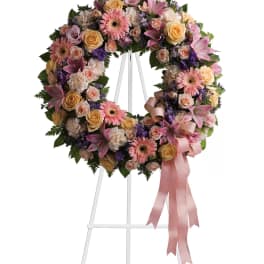 Pastel floral wreath on a white stand with pink ribbon
