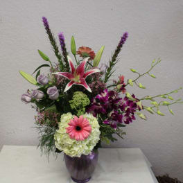 Mixed bouquet in a purple vase with lilies, orchids, roses, and a pink gerbera daisy
