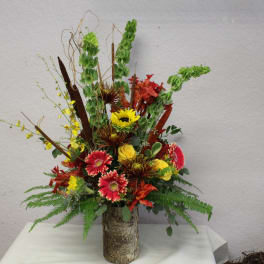 Tall mixed floral arrangement in a textured vase with red, yellow, and green blooms