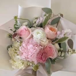 Hand-tied bouquet of pink and white flowers wrapped in pale paper