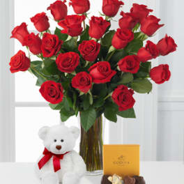 Red roses in a glass vase with a teddy bear and chocolate box