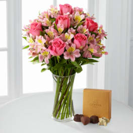 Pink roses and alstroemeria in a clear glass vase with a chocolate box