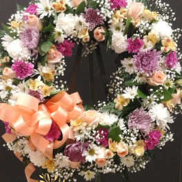 Circular floral wreath with pink, white, and peach flowers on a black stand