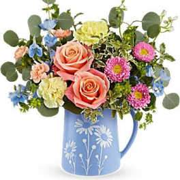 Mixed bouquet of peach roses and colorful blooms in a blue daisy-print pitcher