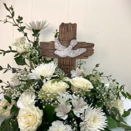 White floral arrangement with roses and daisies around a wooden cross