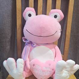 Pink plush frog holding a heart on a wooden chair