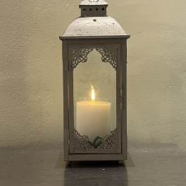 Metal lantern with a lit white pillar candle inside
