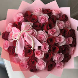 Bouquet of pink and red roses wrapped in pink paper with a pearl bow