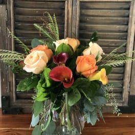 Vase arrangement of peach roses and red and yellow calla lilies in a clear glass vase