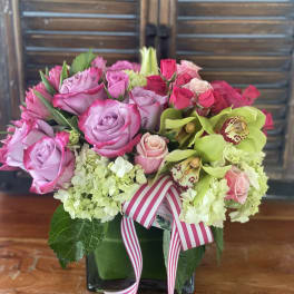 Pink and lavender roses with green orchids in a square vase