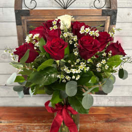 Red roses and white filler flowers in a glass vase with a red ribbon