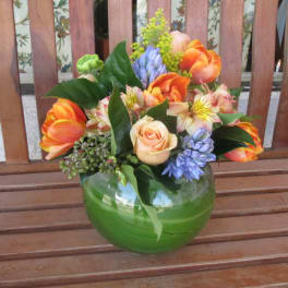 Mixed bouquet of orange, peach, and blue flowers in a green glass vase