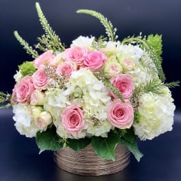 Pink roses and white hydrangeas in a round basket arrangement