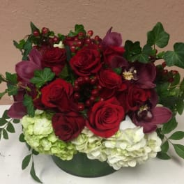 Red roses and purple orchids arranged with hydrangeas in a low container