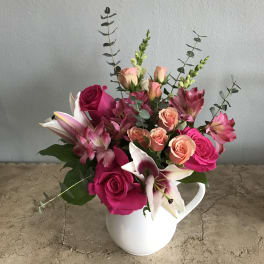 Pink and peach flowers arranged in a white pitcher vase