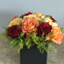 Mixed roses in orange, yellow, and red in a black square vase