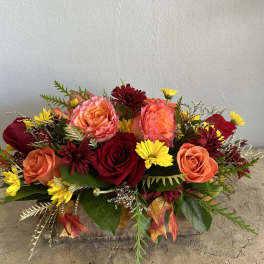 Arrangement of red and peach roses with yellow daisies in a low container