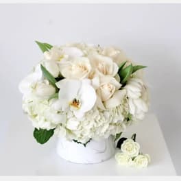 White roses and orchids arranged in a white box with green leaves