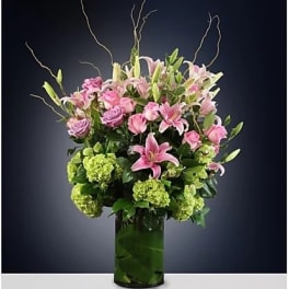 Pink lilies and roses in a tall green glass vase
