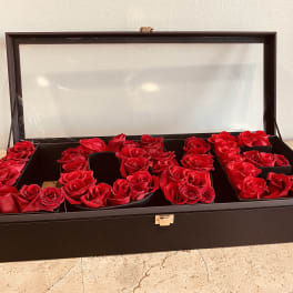 Red roses arranged in a black display box with a clear lid