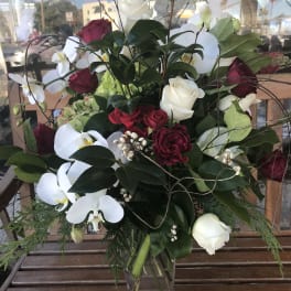 Bouquet of red and white roses with white orchids in a clear glass vase