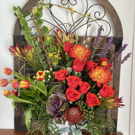 Mixed floral arrangement with red roses, orange dahlias, and tulips in a metal container