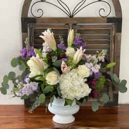 White vase arrangement with lilies, roses, hydrangea, and purple flowers