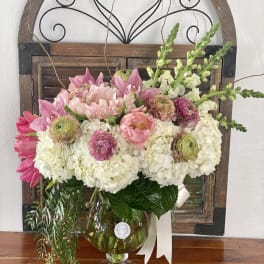 Pink and white floral arrangement in a glass vase with a ribbon