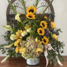 Mixed floral arrangement with sunflowers, lilies, and hydrangea in a metal container