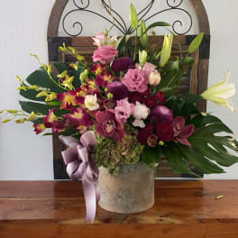 Mixed pink and purple floral arrangement in a stone vase with a ribbon