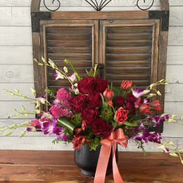 Bouquet of red roses and purple orchids in a black vase with a pink ribbon