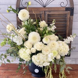Cream floral arrangement in a dark vase with roses, dahlias, and hydrangeas